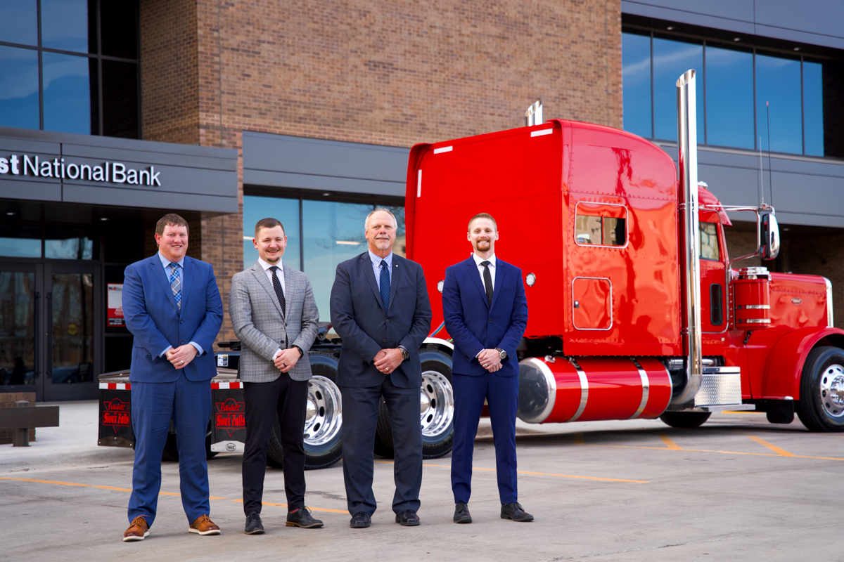 Four men standing in front of a red semi tractor.