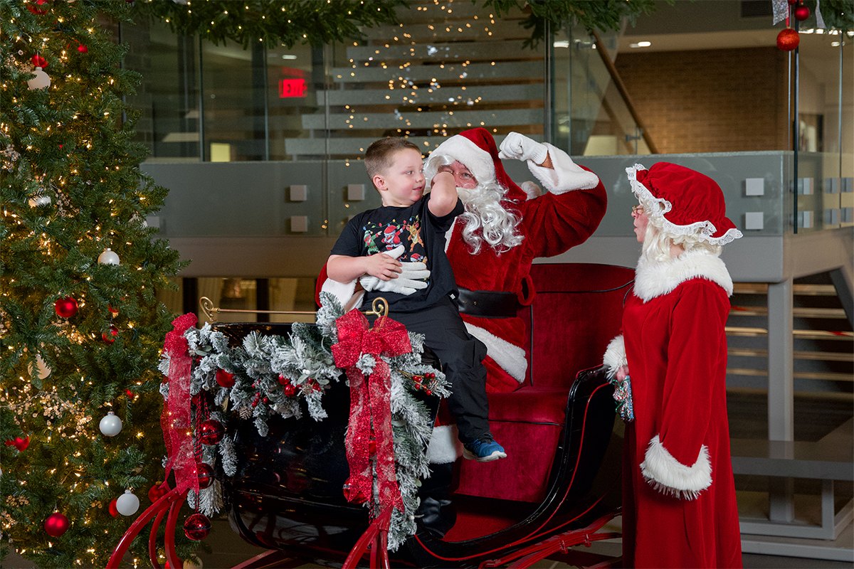 A young boy compares muscle size with Santa while sitting in his sleigh.