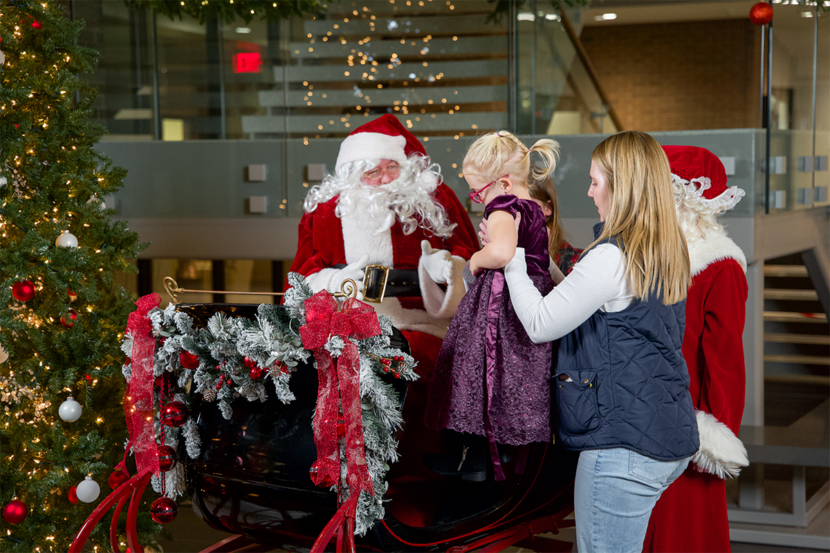 A woman helping a young girl into Santa's sleigh.