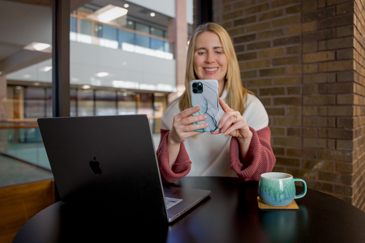 A young woman sitting at a table scrolling on her phone.