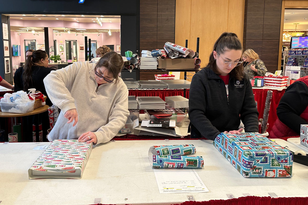 Two women wrapping presents at the Children's Home Society Gift Wrap Booth.