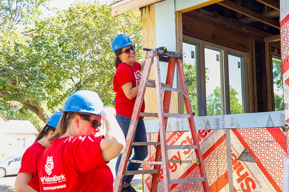 A woman standing on a ladder next to a Habitat for Humanity rehab house.