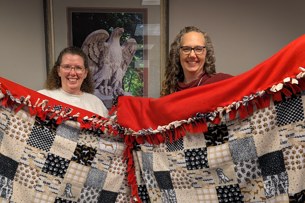 Two women holding up tie blankets for Project Warm-Up.