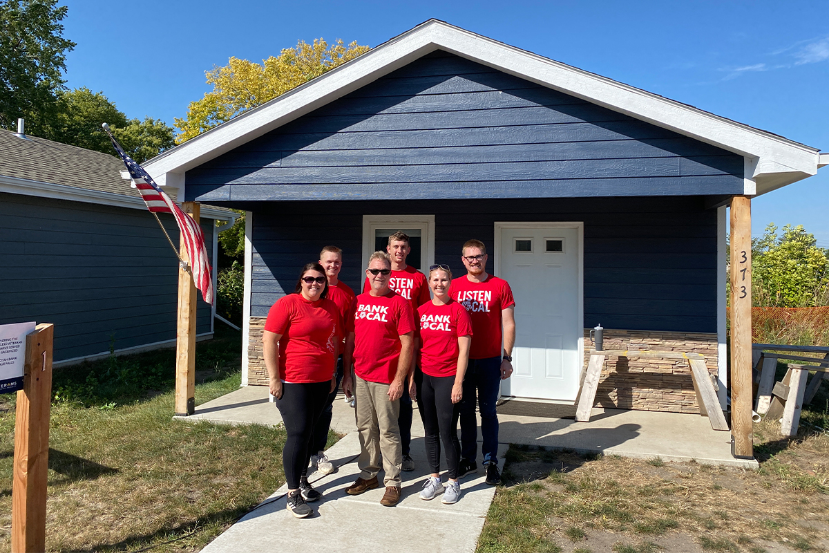 A group of First National Bank teammates standing in front of a tiny house at the Veterans Community Project.