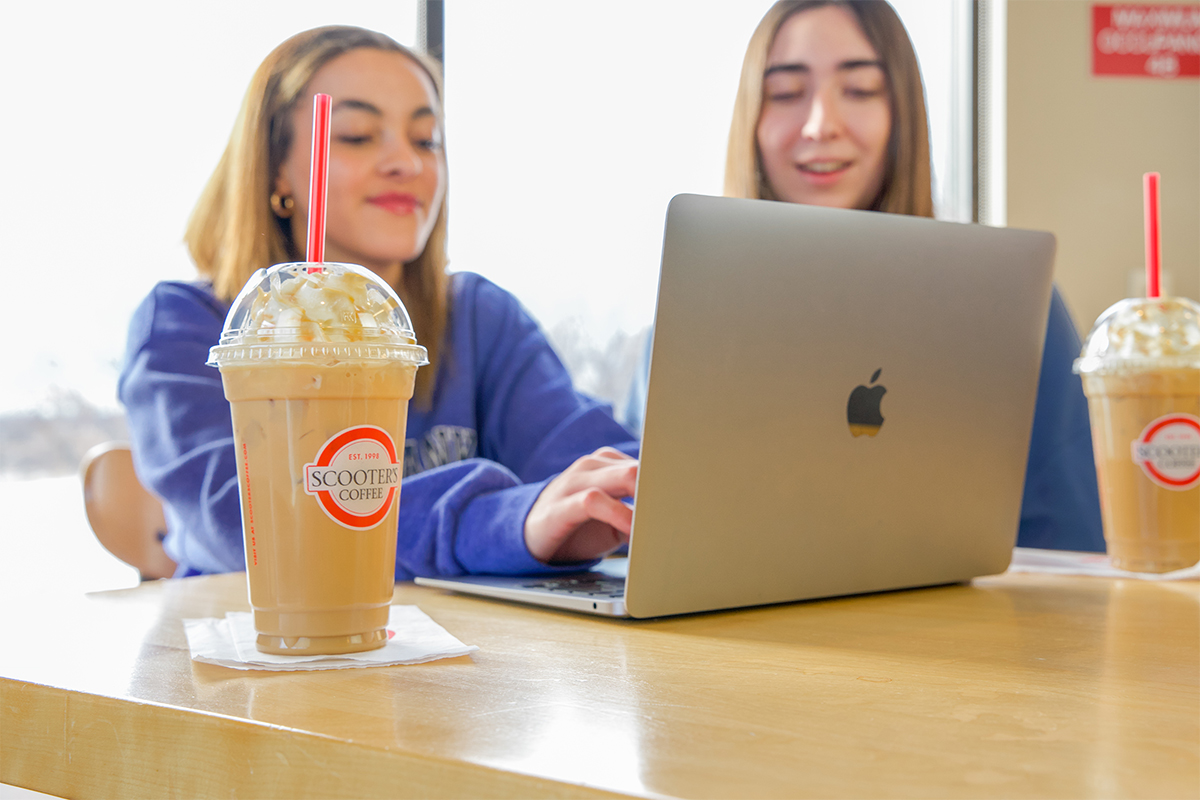 Two high school girls sitting at a table and typing on a laptop.